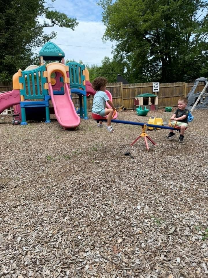 Children playing at a backyard playground with a colorful play structure and seesaw at Mother Goose Day Care