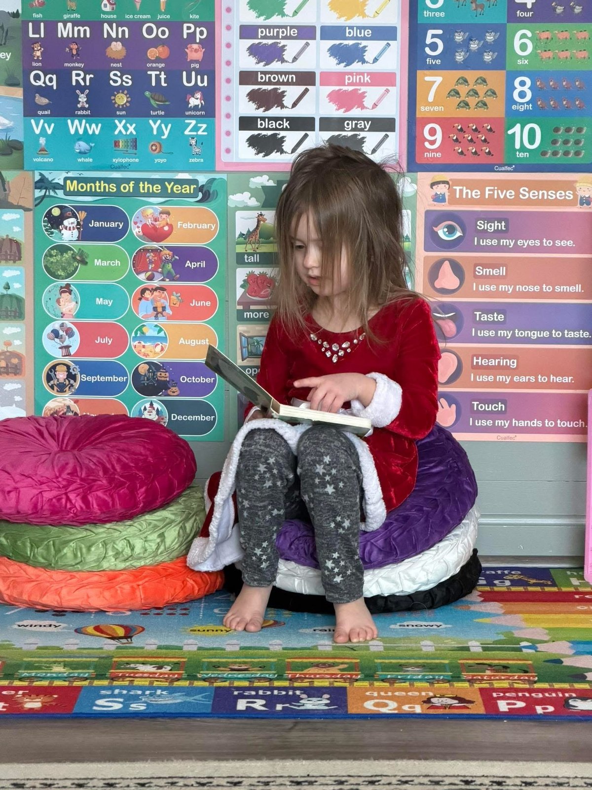 Young girl reading on colorful floor pillows in a bright classroom at Mother Goose Day Care