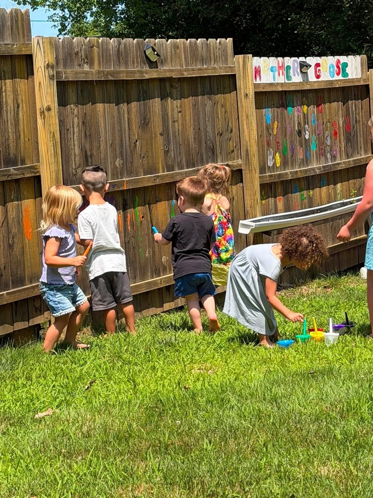 Children painting on a wooden fence in the backyard at Mother Goose Day Care