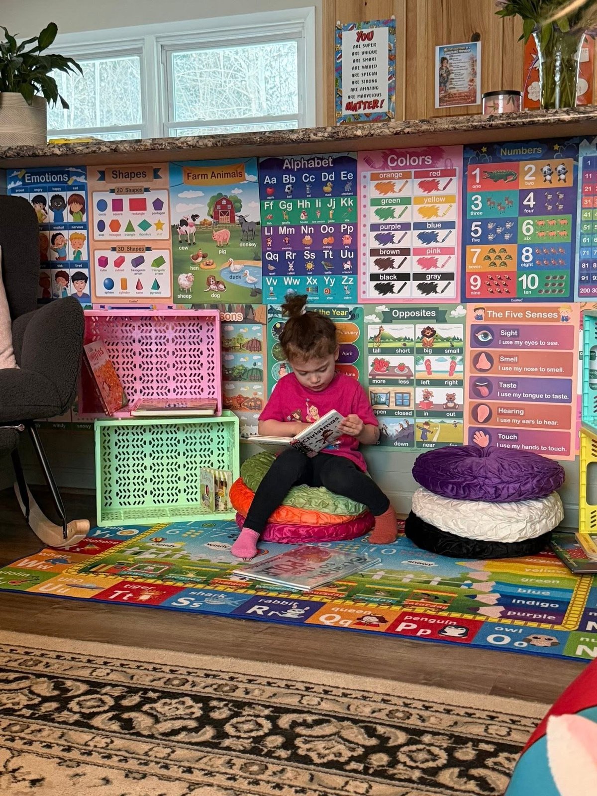 Young child in pink shirt reading on a colorful classroom floor at Mother Goose Day Care
