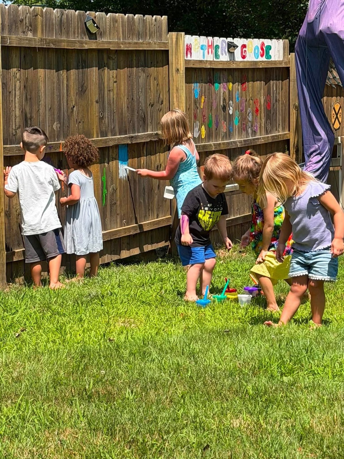 Children drawing on a fence with colorful chalk in the backyard at Mother Goose Day Care
